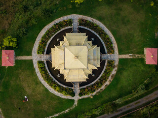 Aerial view of a golden roofed temple surrounded by a circular garden with lush green grass and small structures, Tang Gewog, Bumthang, Bhutan.
