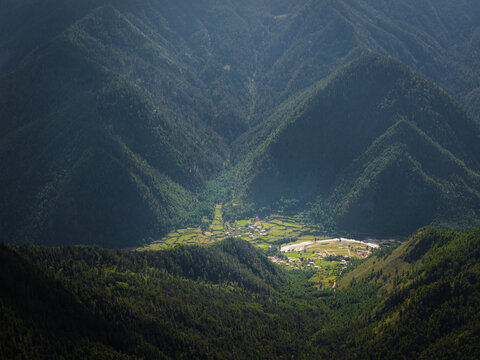 Aerial view of the valley floor dotted with small buildings nestled amidst the towering, verdant mountains, a tranquil scene of nature's embrace, Paro, Paro, Bhutan.