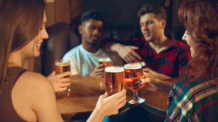 Friends toasting beer glasses with warm light on pub table. Concept of bar promotions, brewery ads, nightlife visuals, beverage marketing assets, and social leisure content.