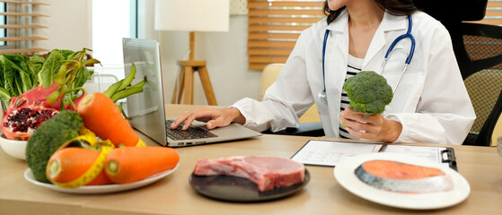 professional nutritionist in uniform writing notes on the table with different healthy products and drawings on the topic of healthy eating