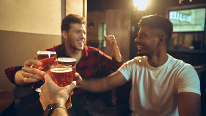 Friends cheering with cold beer glasses at pub table during casual night out. Concept of beverage promotion, pub marketing visuals, nightlife advertising, social drinking culture.