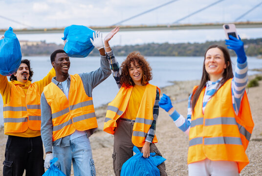 Diverse group of volunteers taking selfie while holding collected trash bags.