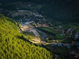 Aerial view of an airstrip nestled in a vibrant valley, flanked by lush green forests and a winding river, Ha, Haa, Bhutan.