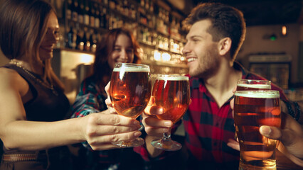 Friends enjoying beer together at bar with shelves of bottles behind them. Concept of bar advertising, brewery marketing, beverage lifestyle visuals, social nightlife.
