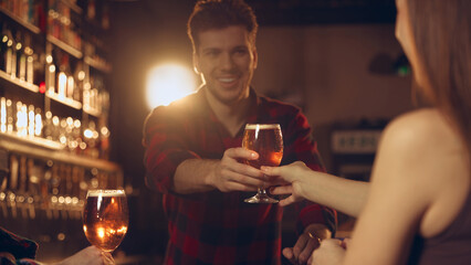 Man handing beer glass to woman during friendly bar gathering. Concept of bar advertising, beverage branding, social nightlife promotion, brewery storytelling.