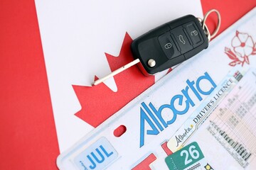 Alberta canadian car license plate and ignition key on flag of Canada close up. Driving permit and registration concept
