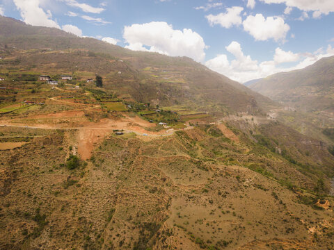 Aerial view of terraced hillsides cascading down towards a valley, revealing a tapestry of earthy browns and muted greens, Raga, Paro, Bhutan.