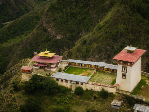 Aerial view of the majestic temple complex perched atop a verdant hill, its golden roofs gleaming against the muted greens and browns of the landscape, Raga, Paro, Bhutan.