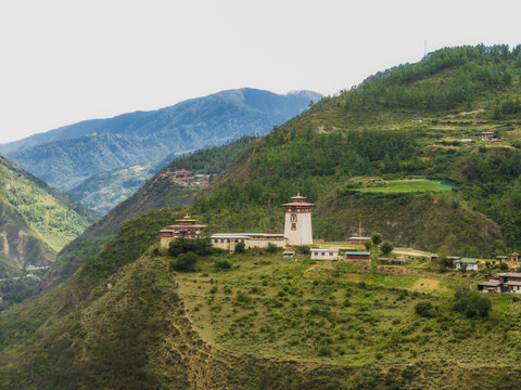Aerial view of a traditional Bhutanese building nestled on a lush green hillside against a backdrop of hazy mountains, Raga, Paro, Bhutan.