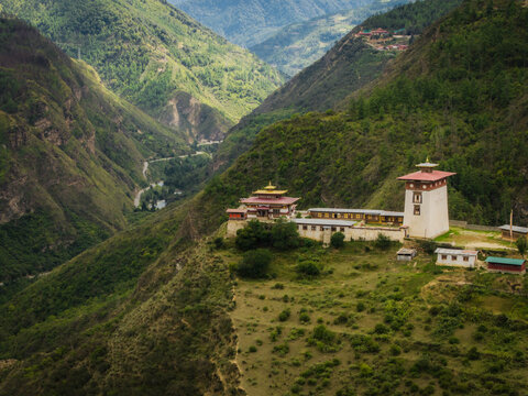 Aerial view of a fortress-like structure with white walls and tiered roofs nestled amid lush green hills, Raga, Paro, Bhutan.