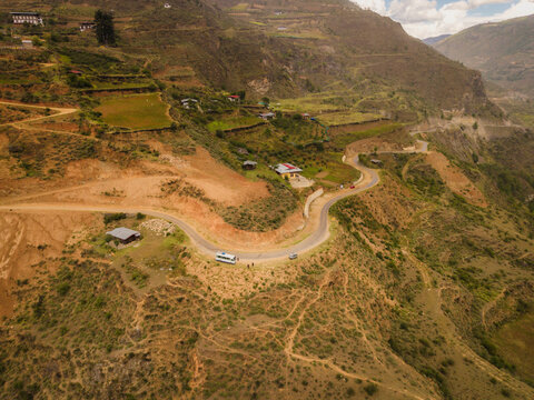 Aerial view of a winding road snaking through rugged, earthy mountainsides dotted with small buildings and terraced fields, Raga, Paro, Bhutan.