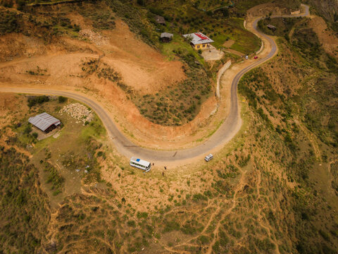 Aerial view of a winding road slicing through the rugged, mountainous terrain, with scattered buildings adding a touch of civilization, Raga, Paro, Bhutan.