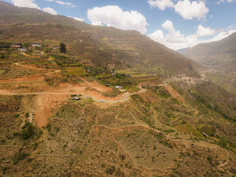 Aerial view of earth tones blending with the lush greens of the mountainside and scattered buildings, Raga, Paro, Bhutan.