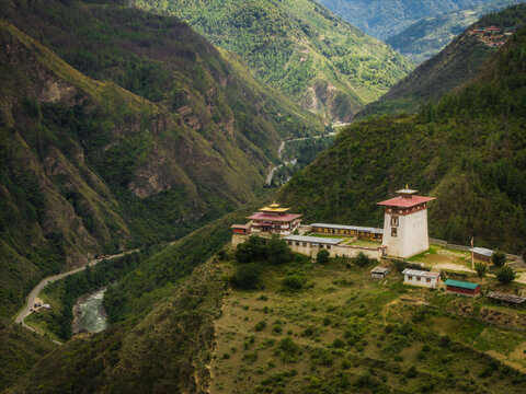 Aerial view of a stunning fortress perched atop a hill, overlooking a winding river cutting through the lush, verdant valley, Raga, Paro, Bhutan.