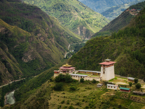 Aerial view of the majestic Paro Rinpung Dzong standing proudly amidst the lush green hills, a serene river winding below, Raga, Paro, Bhutan.