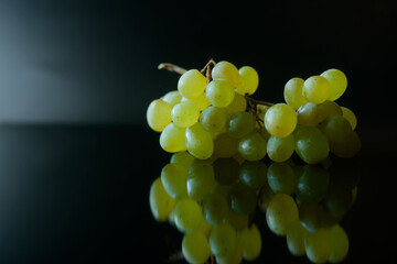 Fresh green seedless grapes bunch on glossy black background with reflection. Ripe sweet organic fruit for healthy vegetarian snack or wine making. Photo