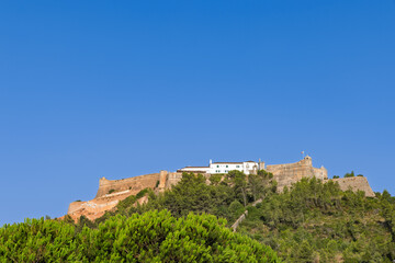 The historic Forte de S&atilde;o Filipe (St. Philip's Fortress) stands atop a lush green hill against a deep blue sky in Setubal, Portugal. Sunny day.