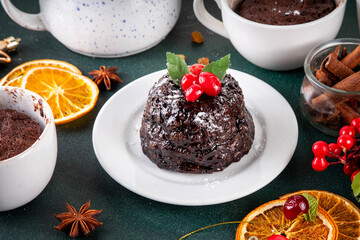 Traditional English Christmas pudding mug cake. Simple Christmas pudding recipe idea, made on tea mug with microwave, portioned Christmas pudding with sugar powder and cranberry festive decor