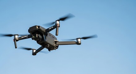 Fototapeta premium A dark gray drone with spinning propellers is captured mid-flight against a clear, bright blue sky.