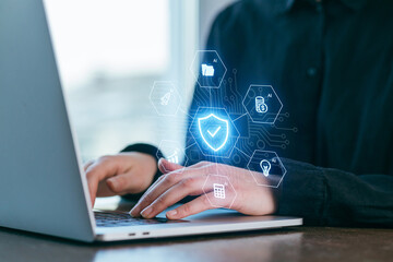 Working on cybersecurity strategies using a laptop with digital icons in a modern office setting during the day