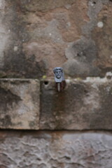 Small sculpted face on a stone wall in Venice, Italy. Ancient textured background with weathered stones and artistic street detail. Mysterious and historical atmosphere.