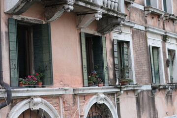 Old Venetian building with open green shutters and flower pots on windowsills. Aged facade with...