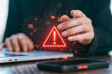 Hands working on a laptop while a warning symbol appears on a digital interface