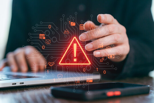 Hands working on a laptop while a warning symbol appears on a digital interface