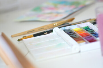 A vivid watercolor set with compact pans, brushes, and a white case rests on a clean studio desk. Ideal for artists, painters, and beginners exploring color and creativity.