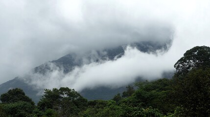 Fototapeta premium Cloudy mountain scenery, with thin mist enveloping the mountains, photographed from a nearby village. The soft, hazy view showcases the rural mountain landscape under a cloudy sky.