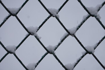 Bliska fotografia siatki ogrodzeniowej pokrytej śniegiem, w tle widać biały, zaśnieżony krajobraz. Zbliżenie podkreśla zimową teksturę metalu i naturalną scenerię. © Adam