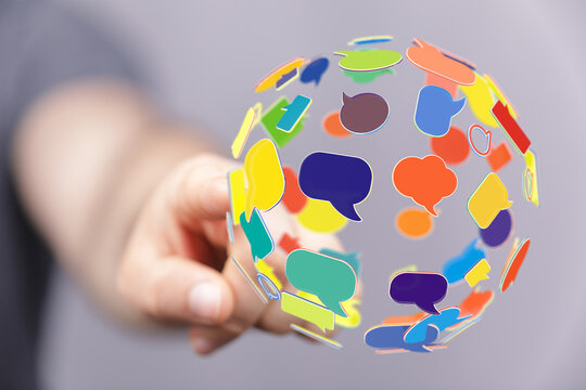 An image of a hand pointing at a sphere covered in colorful chat bubbles. Represents global communication, social media, and digital interaction - Powered by Adobe
