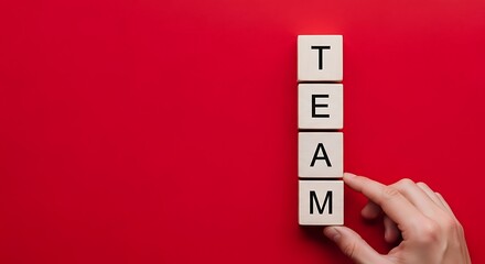 Hand placing the final letter block to spell the word team vertically on a vibrant red background
