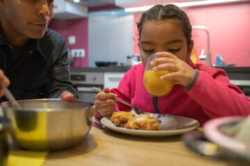 Father and daughter enjoying a casual meal together at home, eating fried chicken and rice while she is drinking orange juice, connecting and bonding over delicious food