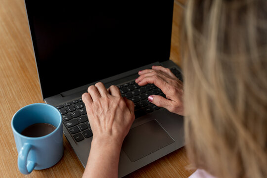 Senior woman hands typing on laptop, working from home with coffee, distant office concept