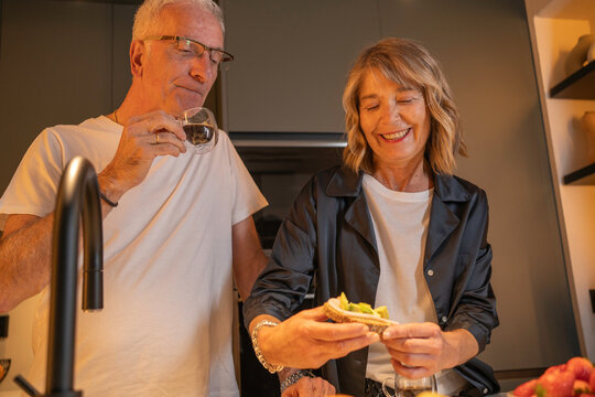 Happy senior couple sharing a healthy breakfast of avocado toast in their modern kitchen - Powered by Adobe