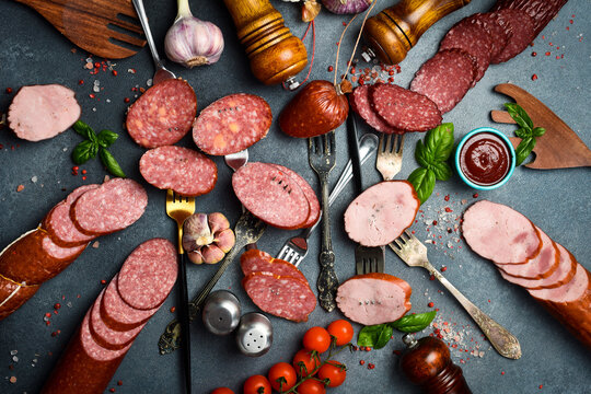 Assortment of different types of salami, paperoni and smoked sausages cut into slices on a dark stone table. Concrete background. Top view.