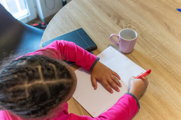 Young child learning and creating, drawing hearts on paper with a red pen at a wooden table, enjoying creative education and personal expression