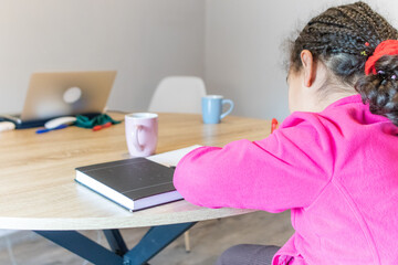 Young person engaged in learning or remote work, leaning over a notebook at a modern wooden table with a laptop, stationery, and hot beverages, emphasizing concentration and productivity