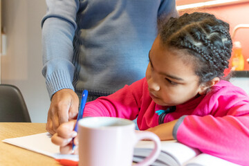 Little girl writing in a notebook, concentrating on her homework, with an adult male's hand gently guiding her in learning and education