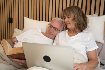 Senior couple sharing a cozy moment in bed, enjoying technology and reading together
