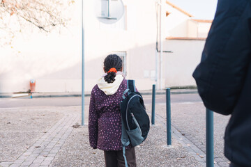 Young student girl with a backpack walking on the street, back to school concept, child on her way to elementary school, beginning of education journey