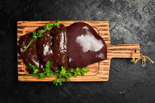 Raw fresh beef liver on a kitchen cutting board. Products with a high iron content. On a black textured stone background.