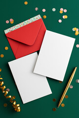 White blank stationery sheets arranged on a green surface, surrounded by colorful confetti and red envelopes, creating a festive atmosphere for invitations or greeting cards