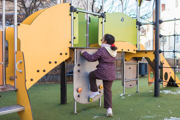 Young girl actively engaging in physical development, learning and overcoming challenges by climbing a playground rock wall at a public park