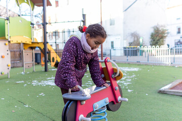Young mixed race girl playing alone on a fun colorful spring rider at a playground, enjoying childhood recreation and activities during daytime in winter