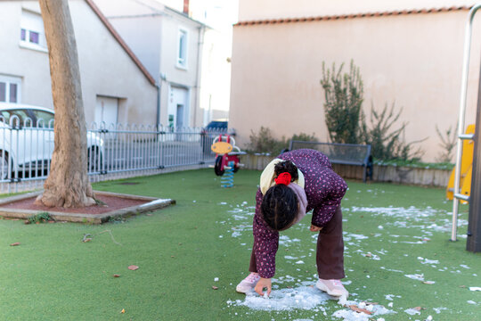 Young girl enjoying winter day playing with snow and ice on green artificial grass playground, experiencing childhood joy and curiosity