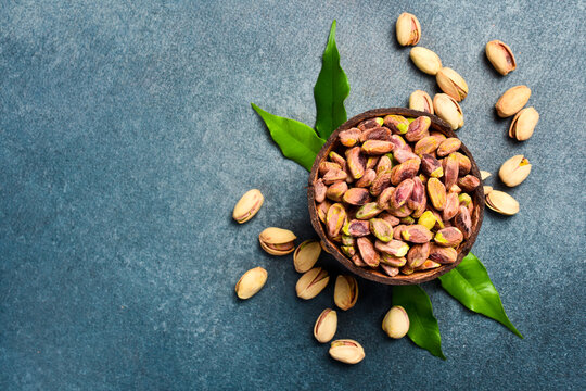 Shelled pistachio kernels in a wooden bowl, ready to eat. On a gray stone background.