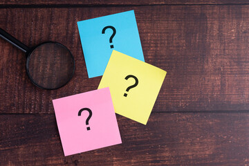 Colorful sticky notes with question marks and magnifying glass on wooden desk.