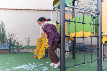 Young girl enjoying active playtime on colorful playground climbing structure during winter, developing motor skills and agility in outdoor recreational fun